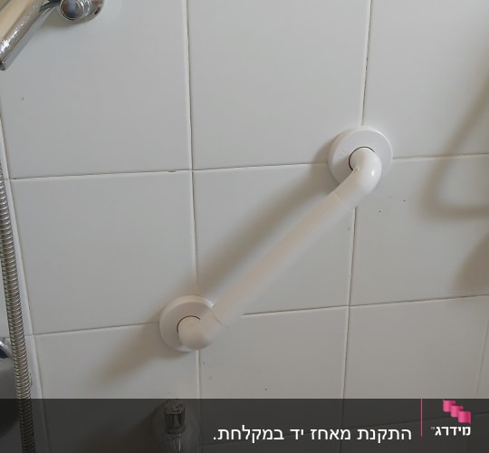מקלחת עם ידית אחיזה על קיר אריחים לבנים